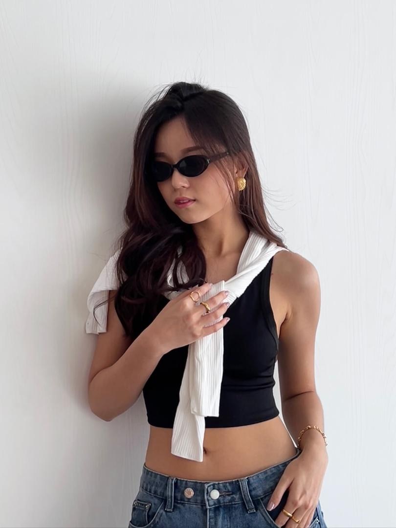 Huan Min in sunglasses and a black outfit, with gold jewellery and a white sweater draped over her shoulders.