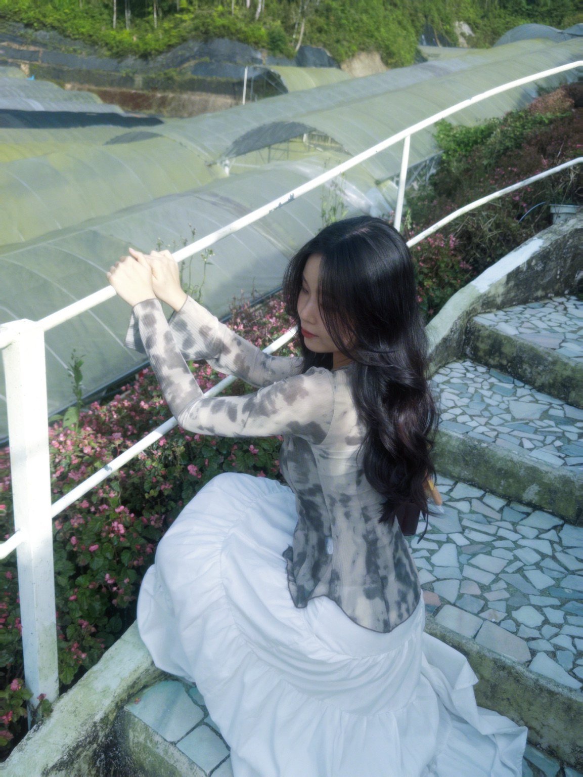 Huan Min wearing a flowing white skirt beside a garden railing, with soft romantic styling.